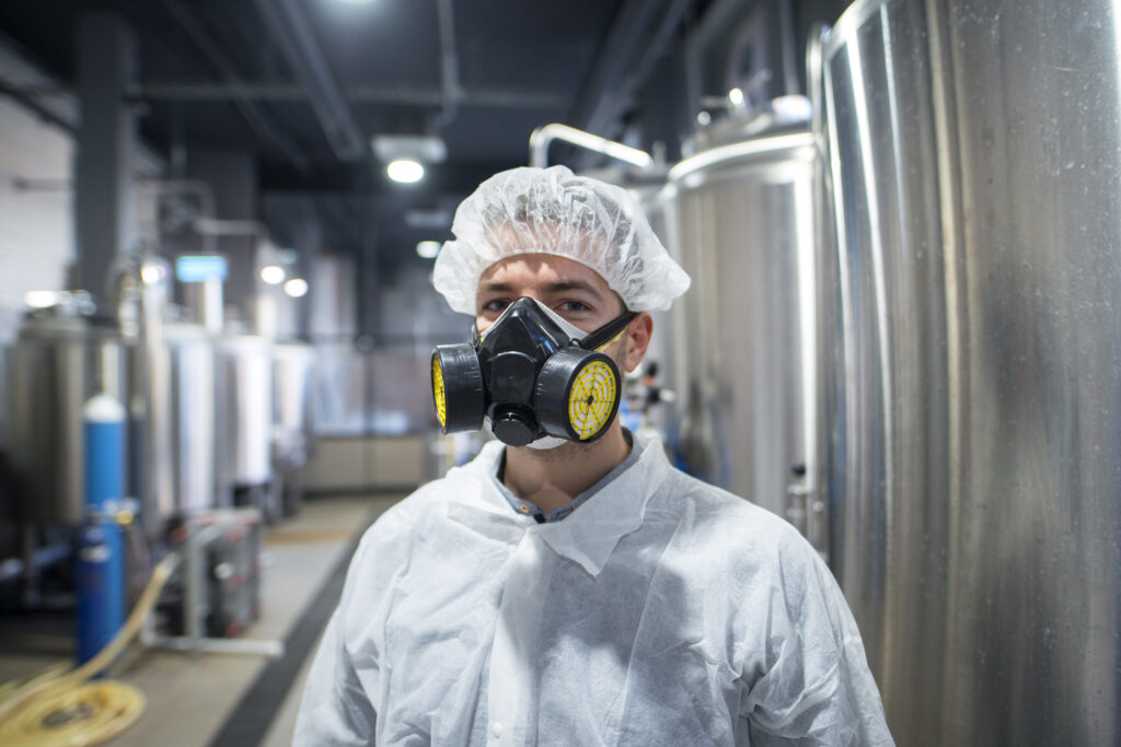 Fachkraft mit Atemschutzmaske und Schutzanzug in einer Industrieanlage